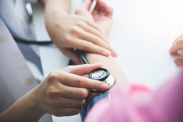 close up of female doctor measuring blood pressure with stethoscope and blood pressure cuff