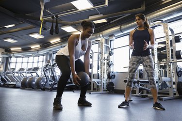 Personal trainer helping woman exercising with medicine ball in gym
