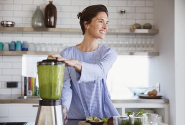 A smiling woman making a green smoothie in a blender