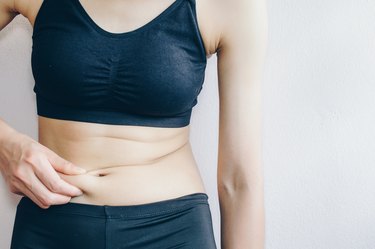 Woman touching her fat belly, woman's hand holding excessive belly fat.