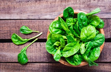 Fresh baby spinach leaves in a bowl on a wooden table.