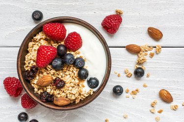 bowl of oat granola with yogurt, fresh raspberries, blueberries and nuts