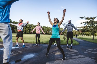 Group of friends doing jumping jacks exercise in a park