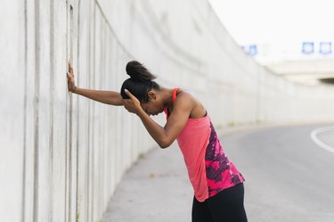 Female runner leaning against a wall after getting a headache