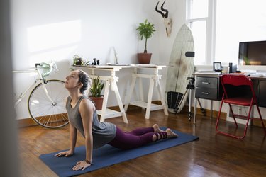 Young Latinx woman practicing yoga upward facing dog pose in apartment