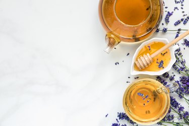 lavender tea in a cup and teapot with honey and fresh flowers over white marble table. herbal drink. top view