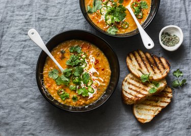 Curried red lentil tomato and coconut soup - delicious vegetarian food on grey background, top view. Flat lay served healthy lunch