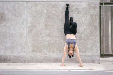 Full Length Of Woman Doing Handstand On Footpath Against Wall
