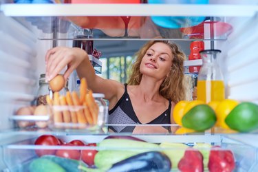 Young Caucasian woman taking egg from fridge.