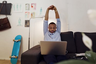 Overwhelmed businessman stretching hands while working on laptop in creative office