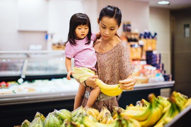 妈妈和蹒跚学步的女孩在超市选择香蕉帮助缺钾