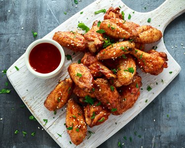 Baked chicken wings with sesame seeds and sweet chili sauce on white wooden board