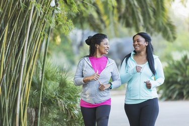 two people in colorful workout clothes in a park walking to lose belly fat