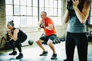 two older adults doing kettlebell exercises in a gym setting
