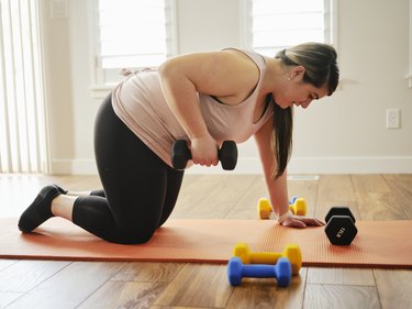 woman doing a dumbbells tricpes kickbacks exercise on a coral exercise mat at home