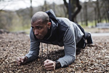 Determined male athlete performing plank position in forest