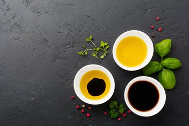 Soy sauce, olive oil and balsamic sauce with herbs basil, parsley, pepper and thyme in white ceramic bowls on black stone or concrete background.