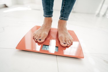 cropped view of a person's feet standing on an orange bathroom scale to determine weight