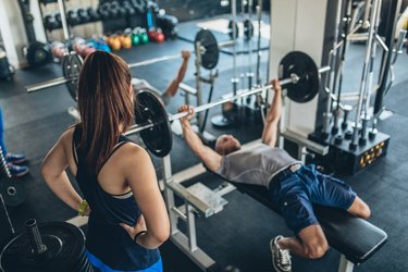 Trainer spotting man and pointing out mistakes while he does a bench press