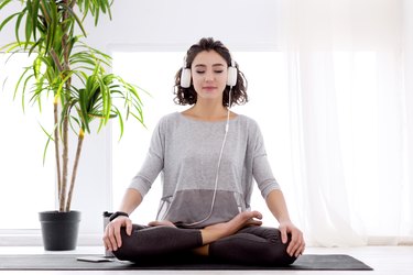 Modern woman with headphones sitting in yoga lotus posture