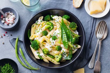 Pasta with green vegetables and creamy sauce in black bowl on grey stone background. Top view.