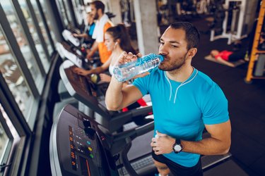 Young man drinking water while exercising on treadmill