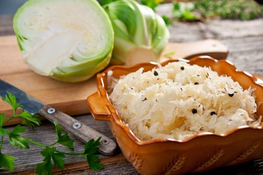 closeup of probiotic sauerkraut in a bowl with sliced cabbage on a wooden cutting board