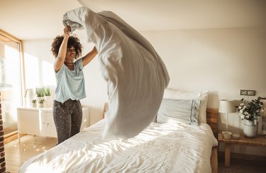 a woman making her bed in the morning, as an example of morning habits for better sleep