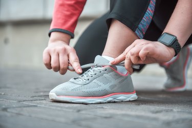 Cropped image of a woman in sports clothing tying shoelace while standing outdoors