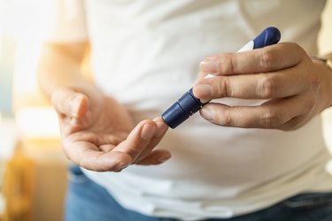 Close up of man hands using lancet on finger to check blood sugar level by Glucose meter. Use as Medicine, diabetes, glycemia, health care and people concept.