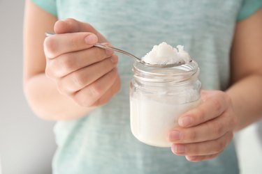 Woman holding jar and spoon with coconut oil, closeup. Healthy cooking