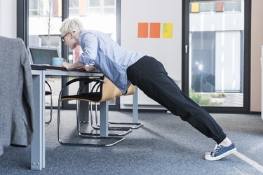 Woman in office doing push-ups on desk