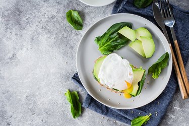 Sandwich with avocado, spinach and poached egg on whole wheat bread on plate on stone background. Helathy Food Breakfast Concept. Top view, copy space