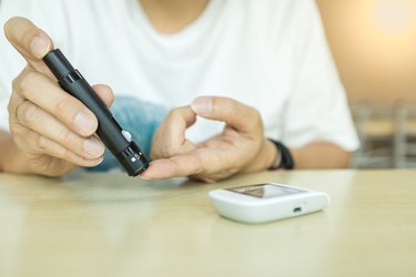 Close up of man hands using lancet on finger to check blood sugar level by Glucose meter. Use as Medicine, diabetes, glycemia, health care and people concept.