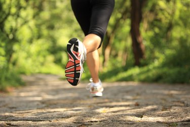 Runner athlete legs running on forest trail.