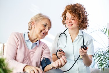 Young nurse measuring blood pressure of older woman.