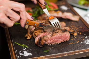 hand holding knife and fork cutting grilled arachidonic acid-rich beef steak