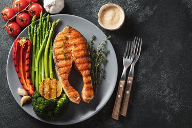 Tasty and healthy salmon steak with asparagus, broccoli and red pepper on a gray plate. Diet food on a dark background with copy space. Top view. Flat lay