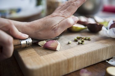 close view of a person peeling garlic on a wooden cutting board