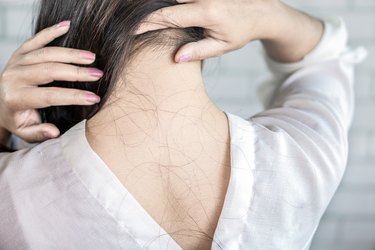 Woman inspecting her scalp, with hair strands falling on her neck and shoulders