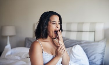 A person wearing pajamas yawning on the edge of their bed, tired after eating a meal.