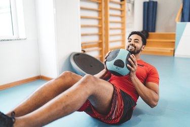 athlete doing one of the best ab exercises holding medicine ball in crunch position on teal floor