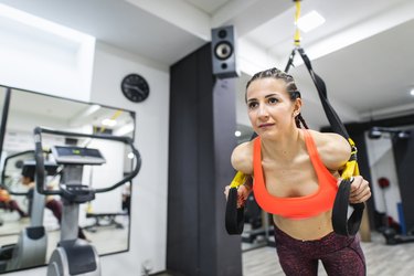 Young sportswoman doing arm exercises with suspension straps