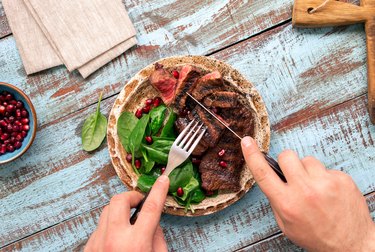 Hand cutting taurine-rich beef grilled steak on wooden table