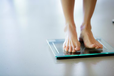 Close-up photo of two feet standing on a glass bathroom scale