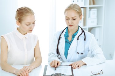 Doctor and patient talking in hospital office while sitting at the desk. Health care and client service in medicine