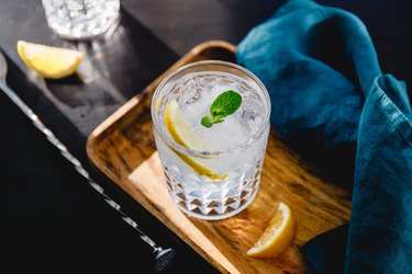 Refreshing cold summer cocktail with soda water, lemon and ice cubes on a wooden tray.