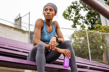 Black woman resting on bleachers, bloated after working out