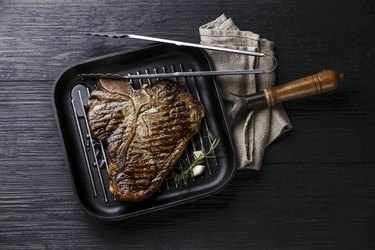 Grilled Dry Aging T-bone steak in grill iron pan and tongs on black burned wooden background