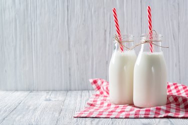 Bottles of milk with red straws and checkered towel on wooden background